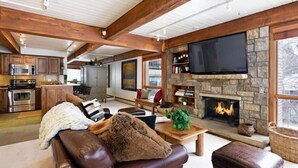 A spacious living room with a stone fireplace, a large flat-screen TV, and a cozy seating area with a leather couch and ottoman. - Snowmass Village 2 Bedroom Platinum-rated Ski In, Ski Out Condo (Snowmass Village)