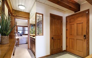 Un pasillo con puertas de madera, una planta en maceta y vista a otra habitación.