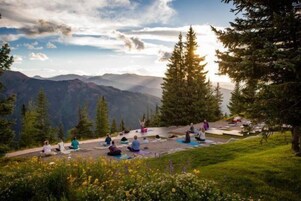 Un grupo de personas meditando al aire libre con montañas al fondo.
