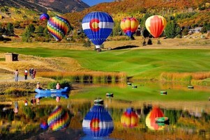Un campo de golf con globos aerostáticos al fondo y una masa de agua en primer plano.