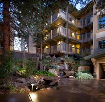 Un hotel de varios pisos con balcones, un jardín ajardinado con una pequeña cascada y un camino de piedra.