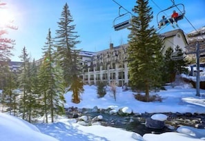A ski resort with a building surrounded by snow-covered trees and a stream. - Gold-rated 3 Bedroom Condo Near Grand Hyatt Vail and Chair Lift 20 (Vail)