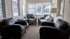 A cozy living room with two leather sofas, a small table, and a lamp. Large windows offer a view of the city.
