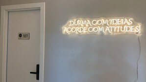 A hotel room with a door labeled "107" and a neon sign on the wall that reads "DURMA COMIDEAS ACORDE COM ATITUDES!"