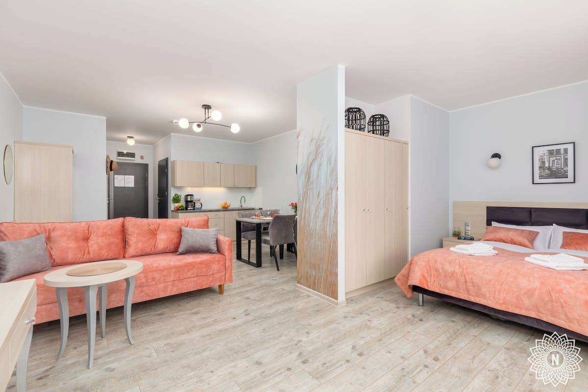 Una habitación moderna y bien iluminada con sofá, una mesita, cama y zona de cocina al fondo.