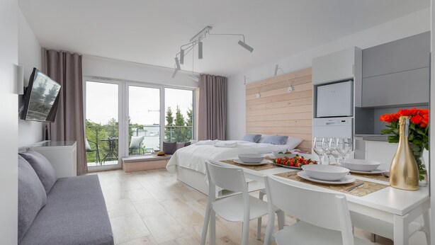 A modern hotel room with a bed, a dining area, a TV, and a balcony with a view. - Seaside Apartamenty - Dominikana (Ustronie Morskie)