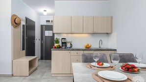 A modern kitchen with light wood cabinets, a built-in oven, and a coffee machine. There is a dining area with a table set for two, a bowl of fruit, and a hat on the wall. - Seaside Apartamenty - Dominikana (Ustronie Morskie)