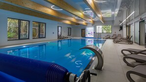 A modern indoor swimming pool with clear blue water, wooden beams, and lounge chairs. - Seaside Apartamenty - Dominikana (Ustronie Morskie)