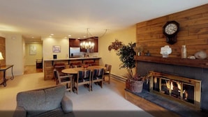 A cozy living room with a fireplace, wooden walls, and a dining area with a kitchen in the background. - 1 Bedroom Boutique Resort Condo With Hot Tub Access and Within Walking Distance to the Eagle Bahn Gondola (Vail)