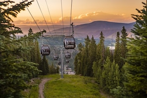 En skidlift med kabiner märkta "Snowmass" mot en bakgrund av berg och träd under solnedgången.