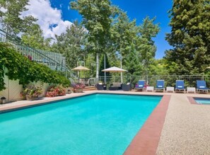 Une piscine rectangulaire dont le bord est recouvert de carrelage, entourée d’une terrasse agrémentée de chaises longues et de parasols.
