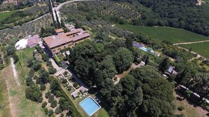 Vue aérienne d’un vaste domaine dont le bâtiment principal est entouré d’une végétation luxuriante, d’une piscine et de champs de vignes.