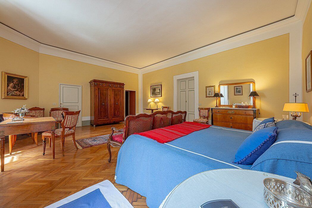 A hotel room with a large bed, a wooden desk, a dining table, and chairs.