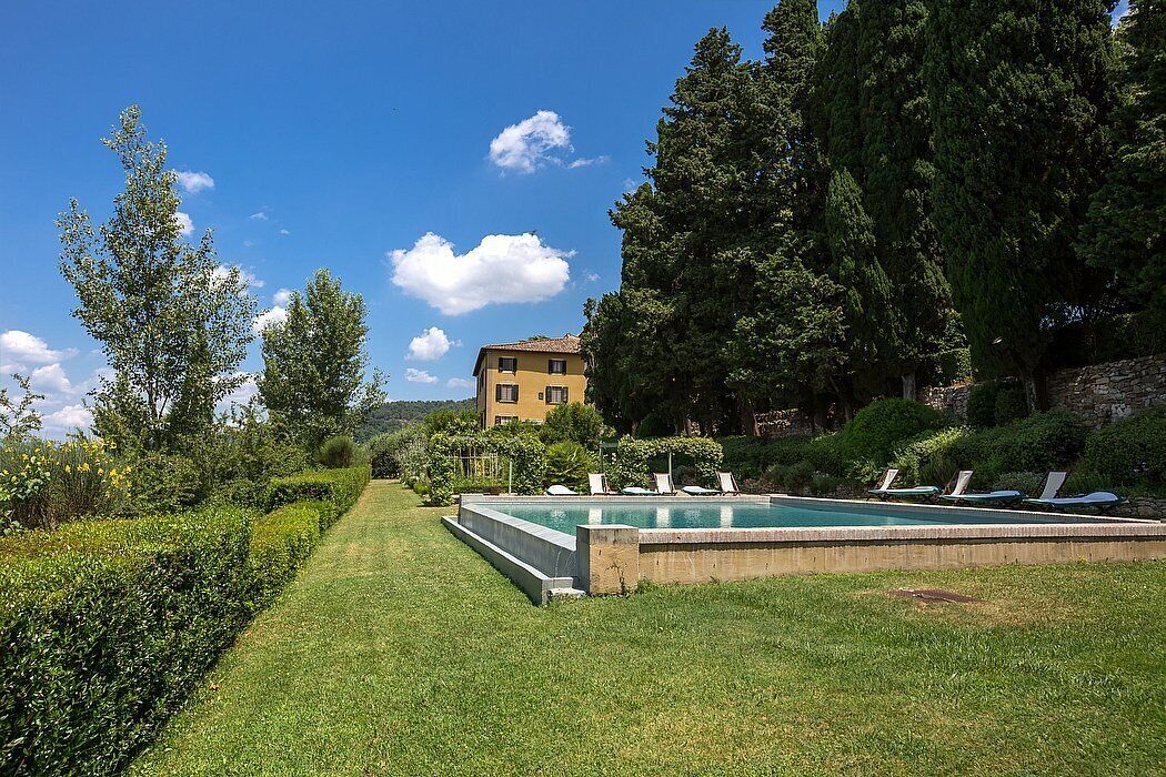 Una piscina con sillas de descanso, un césped bien cuidado y un edificio al fondo.