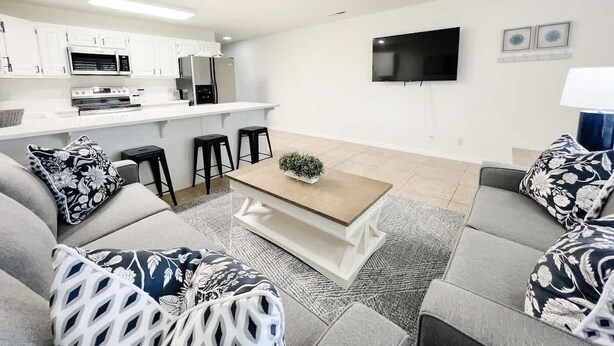 A modern living room with a sofa set, a coffee table, and a kitchen area in the background.