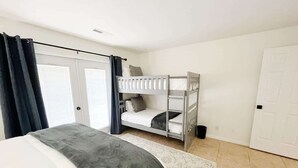 A bedroom with a large bed, a bunk bed, a door, and a window with curtains.