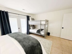Une chambre avec un grand lit, un lit superposé, une porte et une fenêtre avec des rideaux.