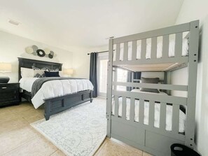 Une chambre à coucher avec un lit, des tables de chevet, une commode, une porte grise et un tapis à motifs.