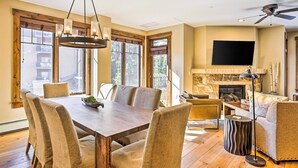 A spacious living room with a large dining table, comfortable seating, a fireplace, and a television.