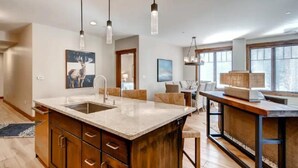 A modern kitchen with a large island, pendant lighting, and a view of the living area.