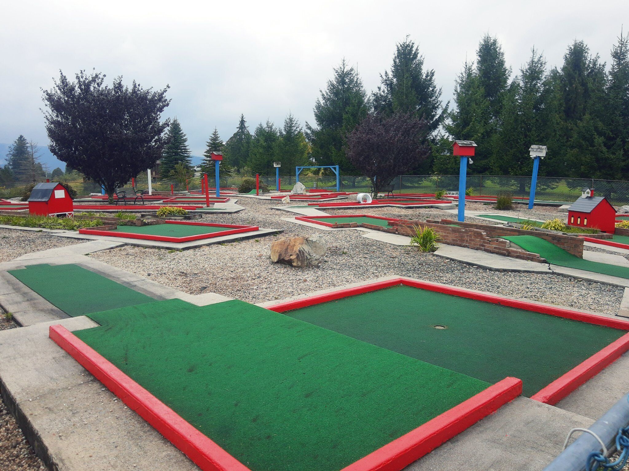 A miniature golf course with multiple holes, red and green turf, and small structures resembling barns.