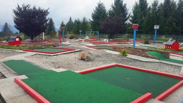 A miniature golf course with multiple holes, red and green turf, and small structures resembling barns.