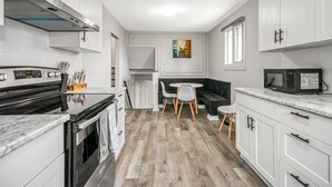 Une cuisine moderne avec des meubles blancs, une cuisinière noire et un four à micro-ondes. On y trouve également un coin repas avec une table et des chaises blanches.