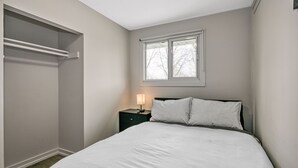 Une chambre à coucher avec un lit, une table de chevet avec une lampe, une fenêtre et un placard.