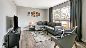 Un salon moderne avec un canapé d’angle, une table basse en verre et un téléviseur à écran plat.