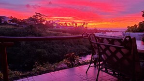 A terrace with a view of a sunset over the ocean, a metal railing, and a chair. - Poipu Beach Kauai Honeymoon: View Sea Turtles From Your Oceanfront Deck-AC (Koloa)