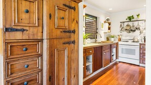 A kitchen with wooden cabinetry, a white stove, and a hanging pot rack. - Poipu Beach Kauai Honeymoon: View Sea Turtles From Your Oceanfront Deck-AC (Koloa)