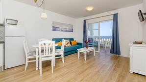 A modern living room with a sofa, chairs, a small table, and a balcony with a view. - Lovely 2-bedrooms condo just 300 mts from beach (Arenal d`en Castell)