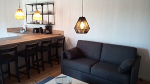 Un ambiente compatto con un divano grigio scuro, un tavolo da pranzo in legno con sedie e lampade a sospensione.