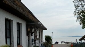 Un edificio con facciata bianca e tetto di paglia, un molo che si protende sull'acqua, e una coppia che passeggia lungo il molo.