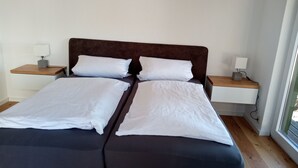 Un letto matrimoniale con lenzuola bianche, una testiera imbottita marrone e due comodini con lampade.
