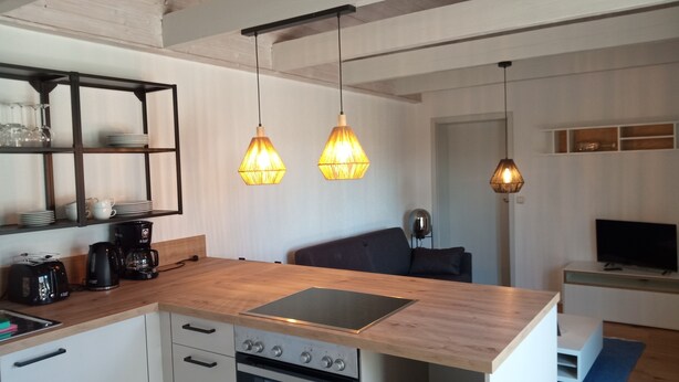 Una cucina moderna con un piano di lavoro in legno, scaffali a scomparsa e luci a sospensione.