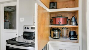 Une cuisine compacte équipée d’un four encastré, d’un four à micro-ondes et d’une cuisinière. Des étagères en bois, situées au-dessus de la cuisinière, servent à ranger un autocuiseur, une machine à café et un mixeur.