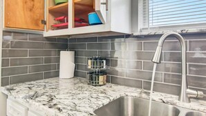 Une cuisine dotée d’un plan de travail en marbre, d’un évier en acier inoxydable et d’un meuble en bois contenant des boîtes de rangement colorées.