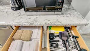 Une cuisine avec un four à micro-ondes posé sur un plan de travail en marbre, un tiroir contenant des serviettes et un autre tiroir contenant des ustensiles de cuisine.