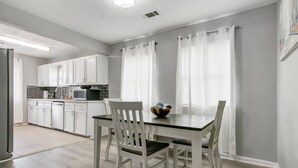 Une cuisine moderne avec des meubles blancs, une table à manger avec des chaises et un saladier posé sur la table.