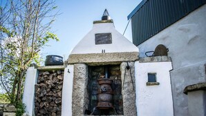 A rustic building with a stone chimney, a stack of firewood, and a large metal pot. - The Heights & Hollows Farmhouse (Downpatrick)