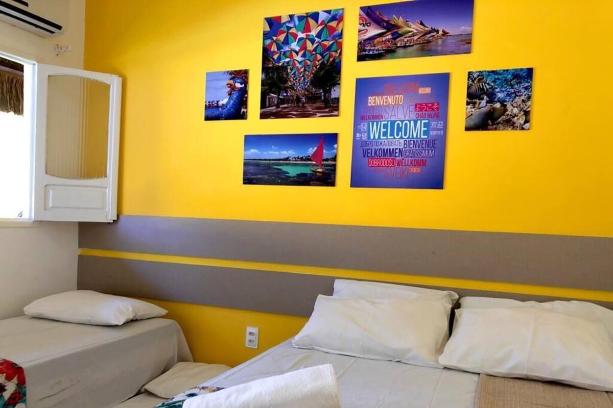 Une chambre d’hôtel avec deux lits, une grande fenêtre et un mur décoré de posters sur le thème du voyage.