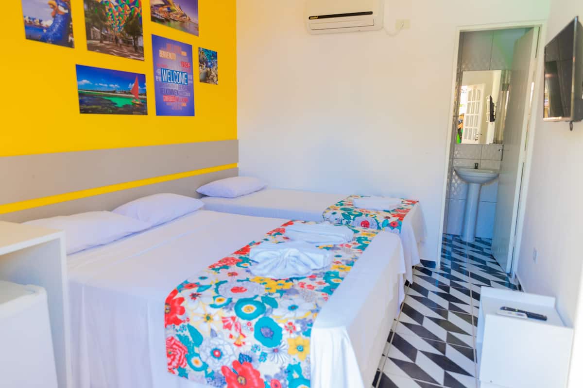 Une chambre d’hôtel avec un lit, une table de chevet, un miroir et une salle de bain visible à travers une porte ouverte.