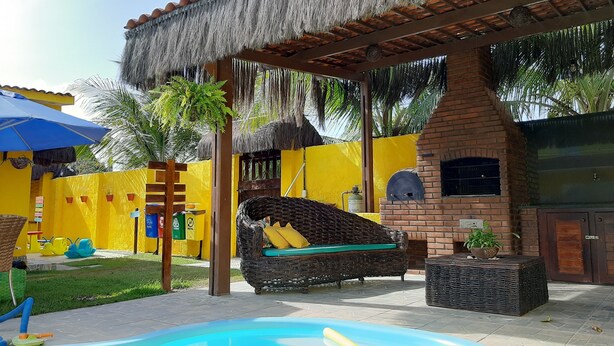 A pool area with a thatched roof structure, a brick oven, and a yellow wall. - POUSADA SUMMER BEACH BY AFT (Ipojuca)