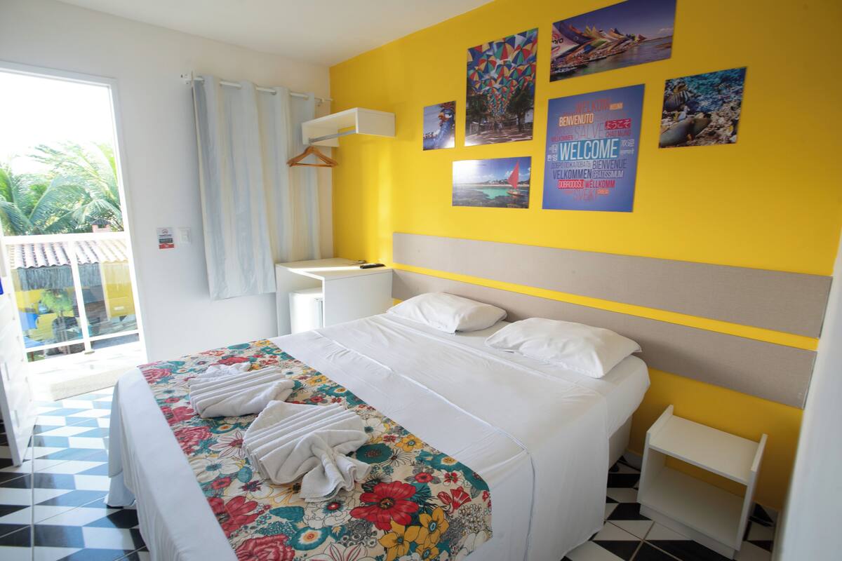 Une chambre d’hôtel avec un lit, une petite table de chevet, un mur décoré de tableaux et une vue sur l’extérieur.