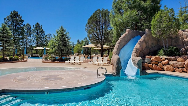 Un área de piscina con tobogán de agua, sillas de descanso y un pabellón.