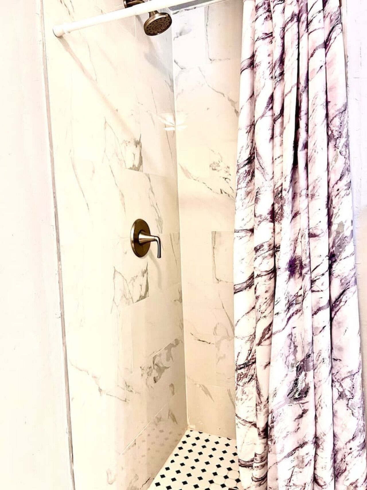 Une douche avec un mur en marbre et un pommeau de douche.