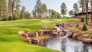 Un campo de golf con un estanque, árboles y un edificio al fondo.