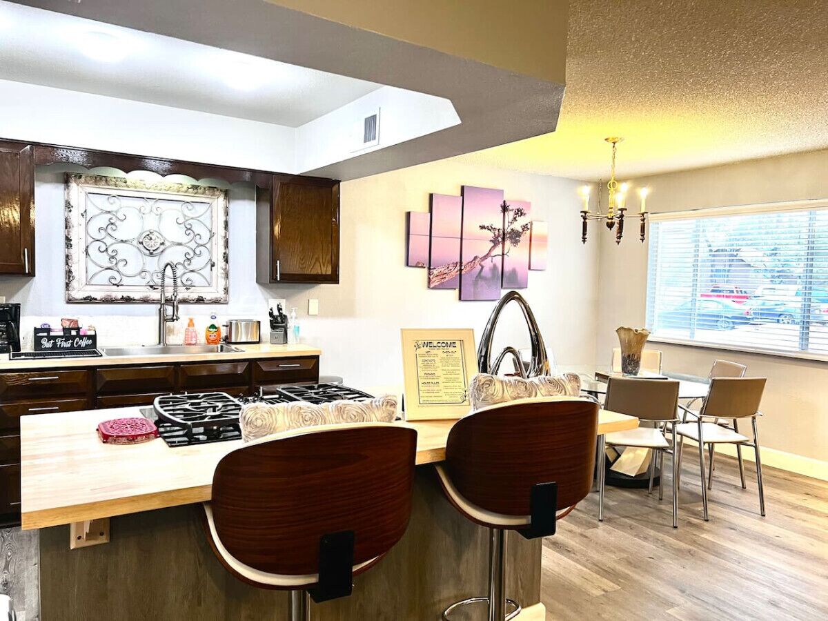 Una cocina moderna con una isla central, taburetes de bar, un letrero de bienvenida y vistas a la calle a través de amplios ventanales.