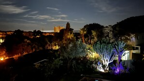 A nighttime view of a landscaped area with illuminated plants and distant buildings. - Luxurious sea view villa for 6 people, 1km from the beach (Marbella)